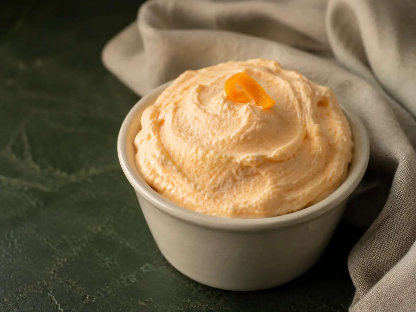 Pale orange creamsicle protein fluff in a small cream stoneware cup with a curl of orange zest.