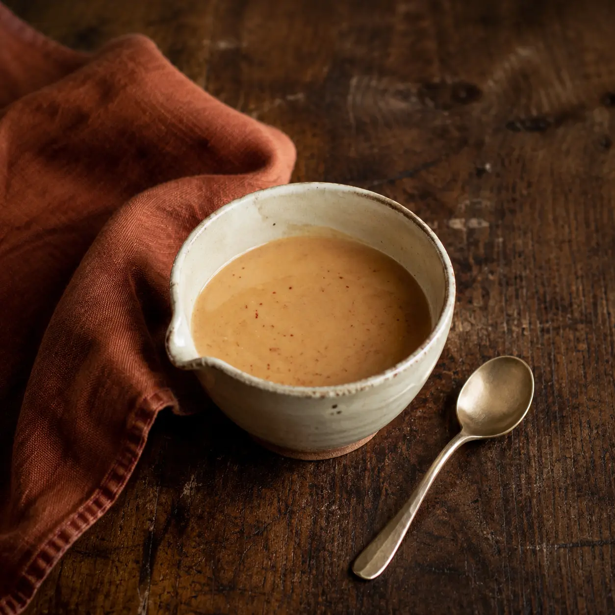 Creamy Szechuan peanut dressing in cream stoneware beside muted-rust linen.