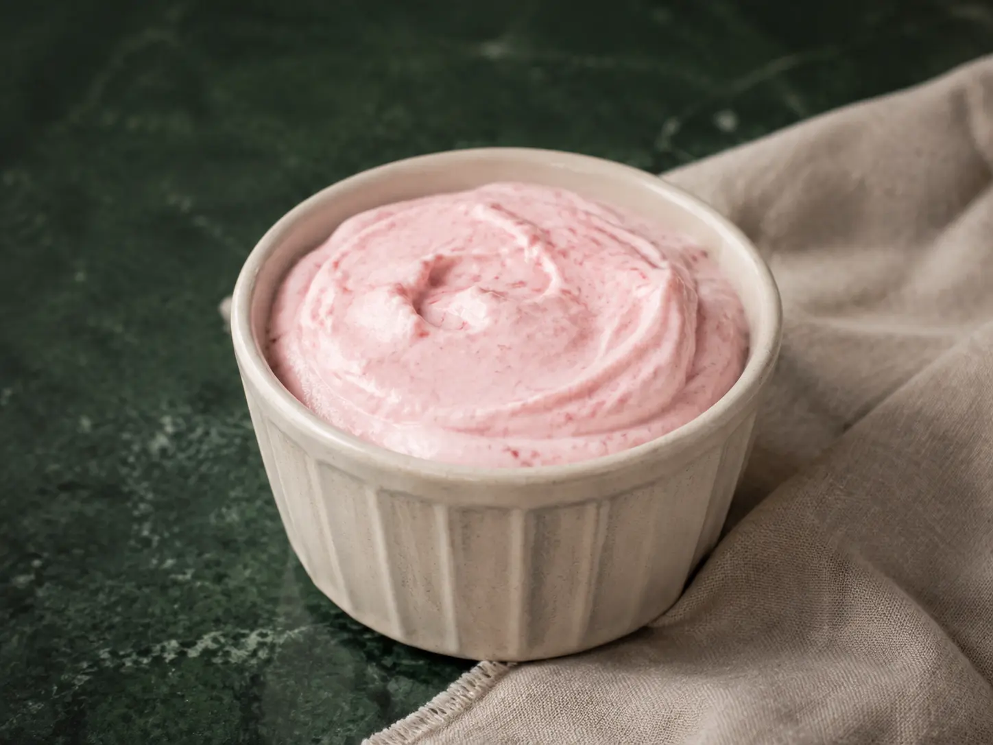 Soft pink strawberry cheesecake protein cloud in a small cream stoneware cup with finely mashed berries.